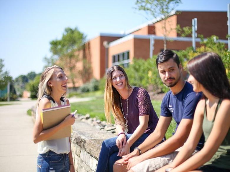 students on campus sitting on the wall outside 体育运动 building